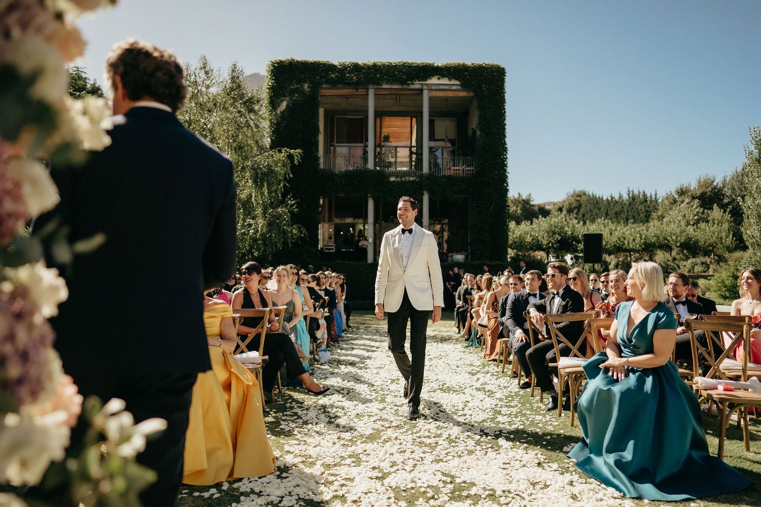 Wedding guests throw white flower petals during an outdoor garden ceremony celebration.