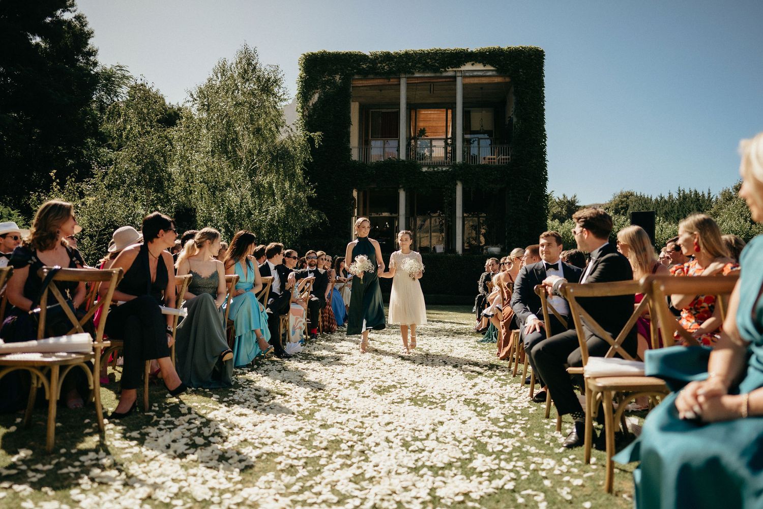 Wedding ceremony guests toss white flower petals in celebration at an outdoor venue.