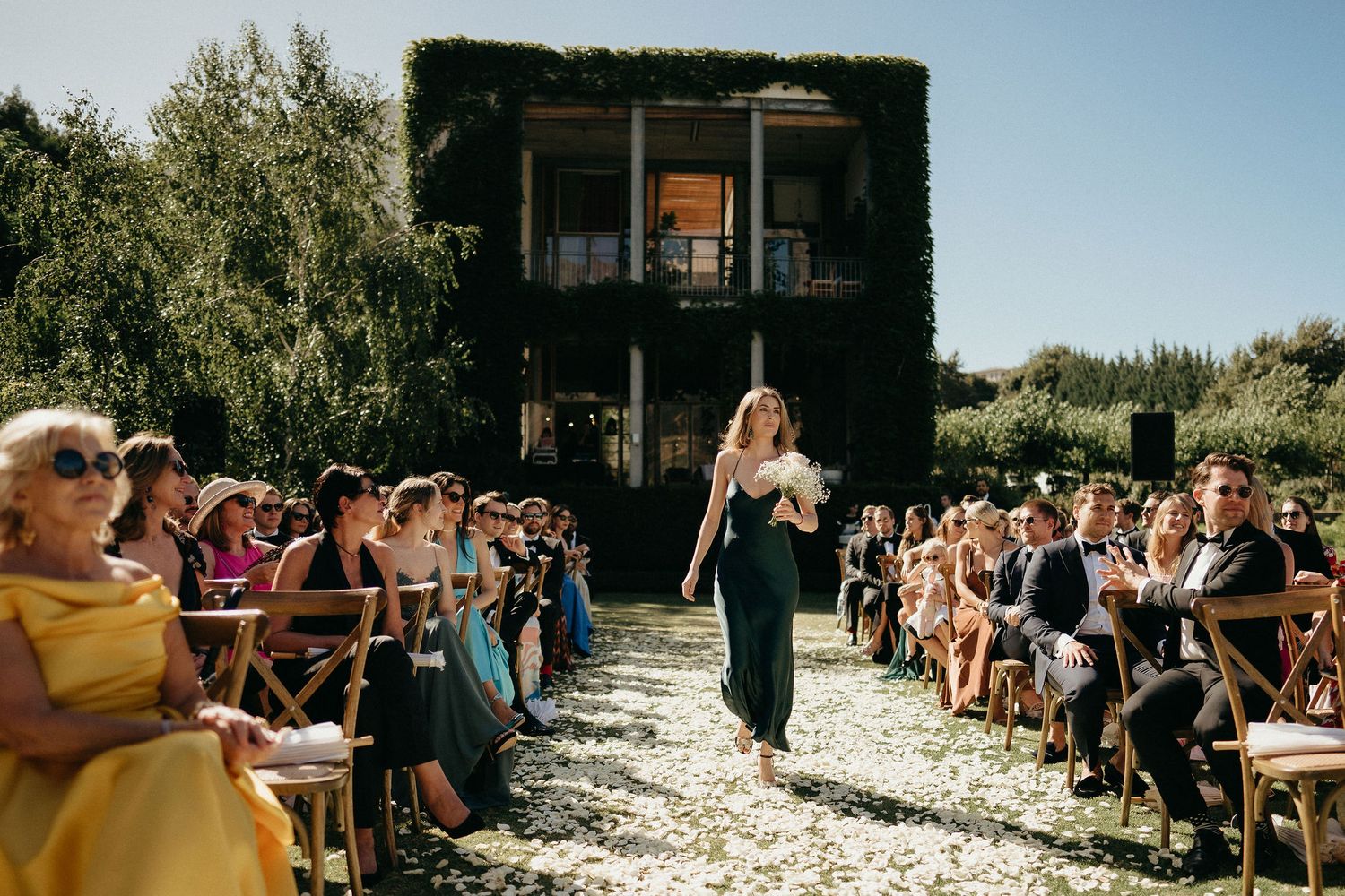 Rustic outdoor wedding venue with wooden cross-back chairs arranged in rows along a stone pathway.