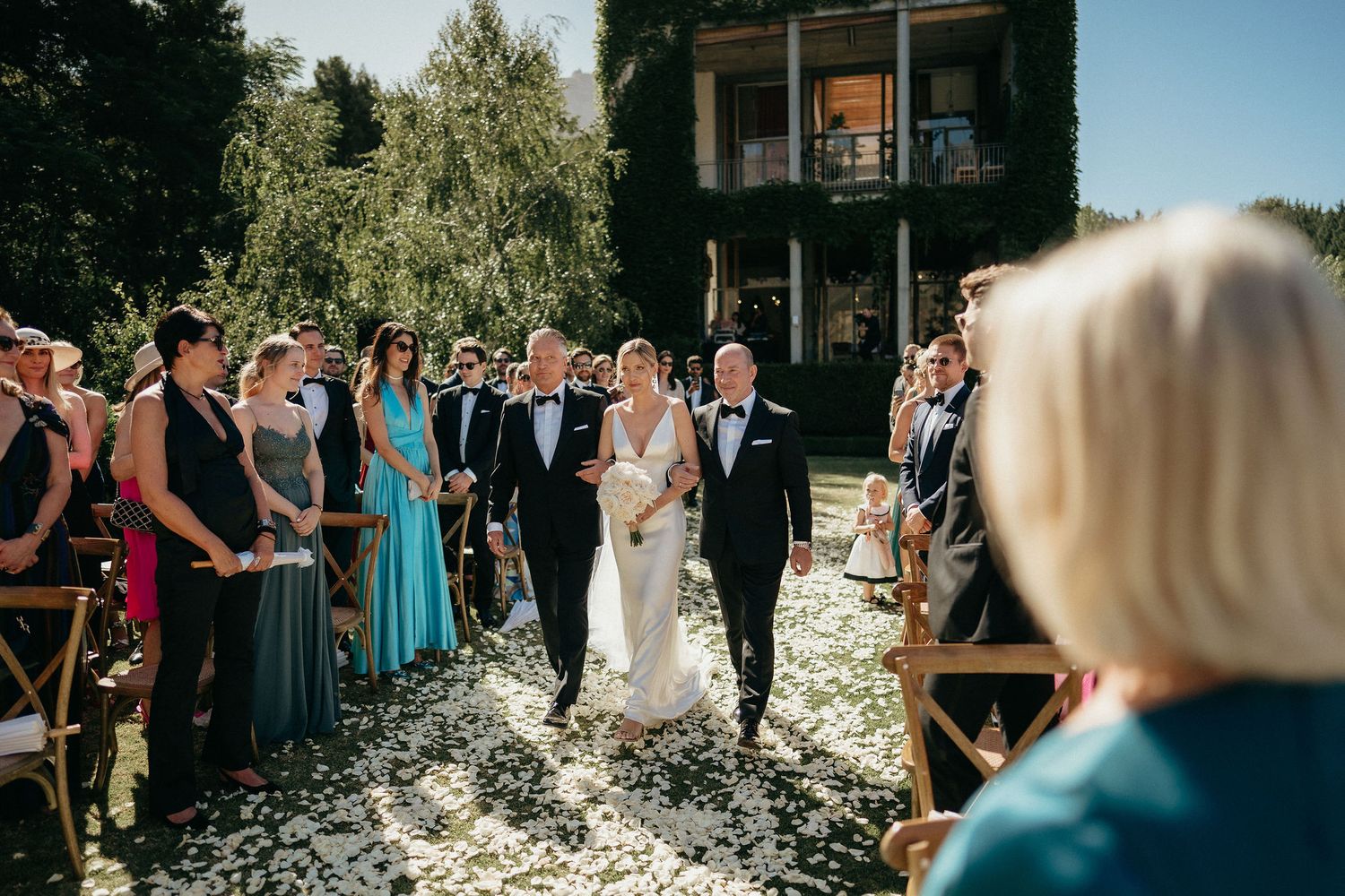 Wedding guests celebrate with confetti and joy during an outdoor ceremony on a sunny day.