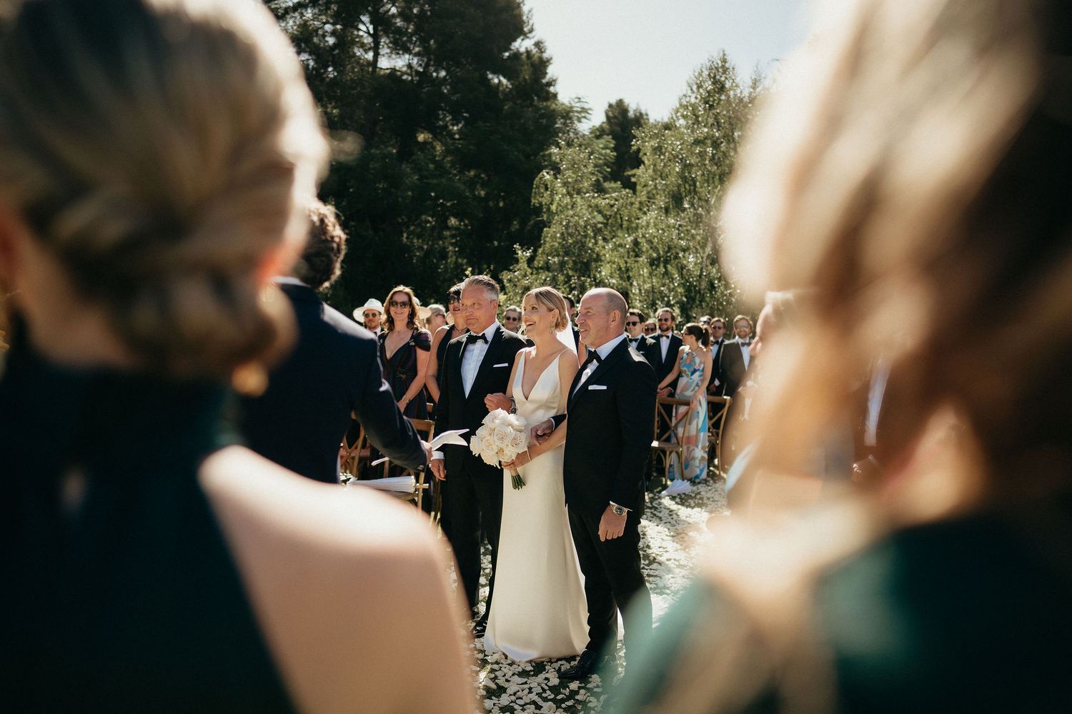 Wedding guests celebrate and dance together during an outdoor reception in a garden setting.