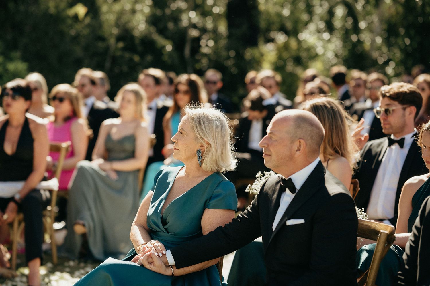Wedding guests dance and celebrate together on an outdoor dance floor during a sunny daytime reception.