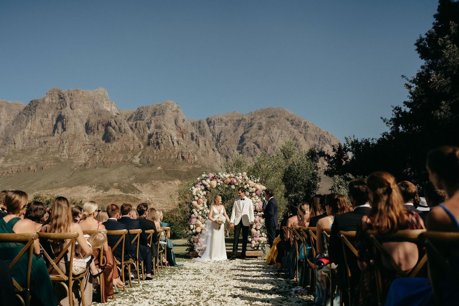 Scenic outdoor wedding ceremony in a desert location with rocky mountain backdrop and wooden chairs arranged in rows.
