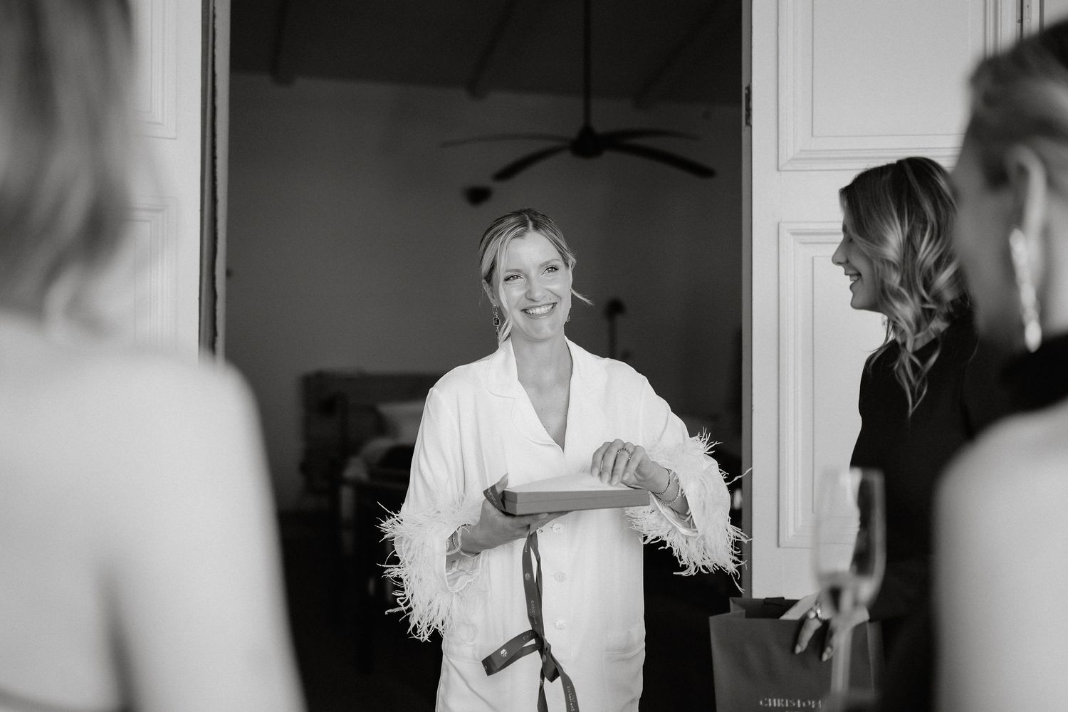 A black and white photo showing someone in a white robe with feather trim during wedding preparations.
