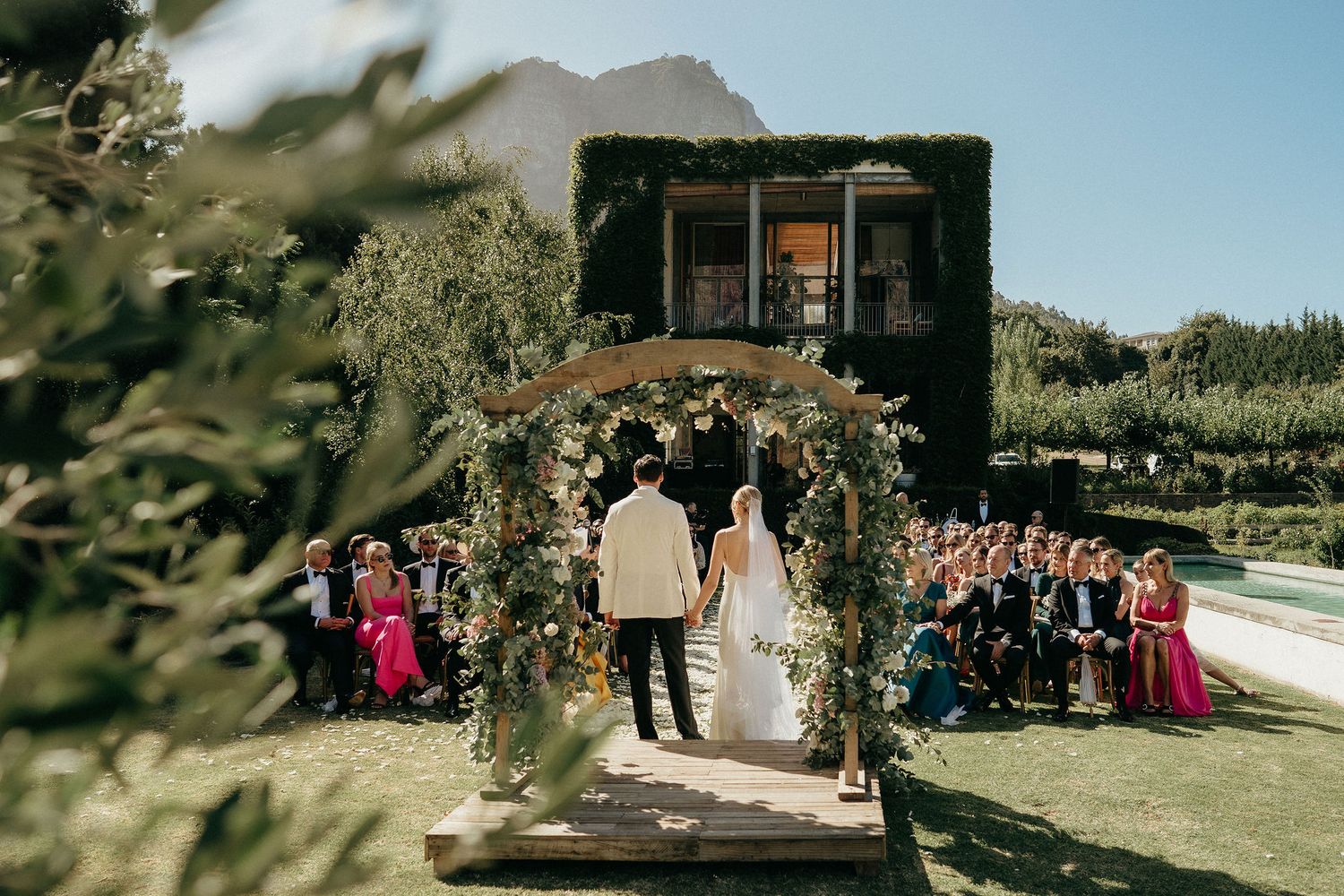 Wedding guests seated outdoors at a rustic venue with mountains and blue skies in the background.