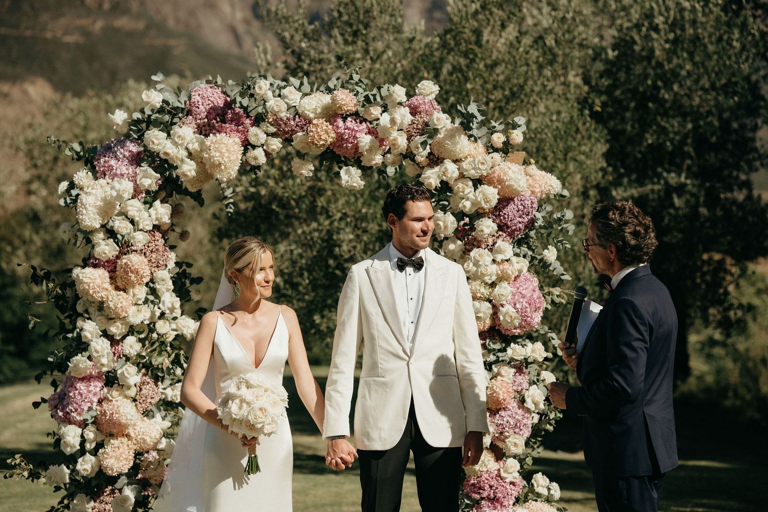 Wedding ceremony setup with pink and white floral arch arrangements in an outdoor garden setting.