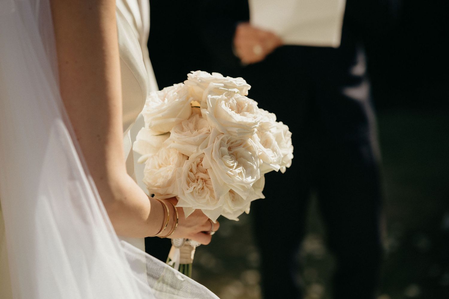 Bride holding a delicate white and blush bouquet during wedding ceremony with soft natural lighting.