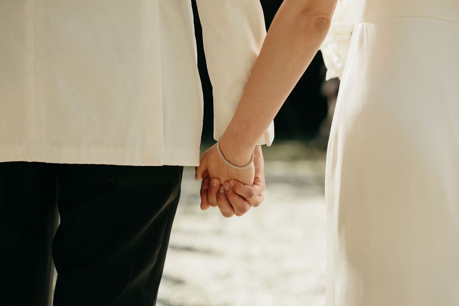 Close up of two people holding hands during a wedding ceremony, with white and black formal attire visible.