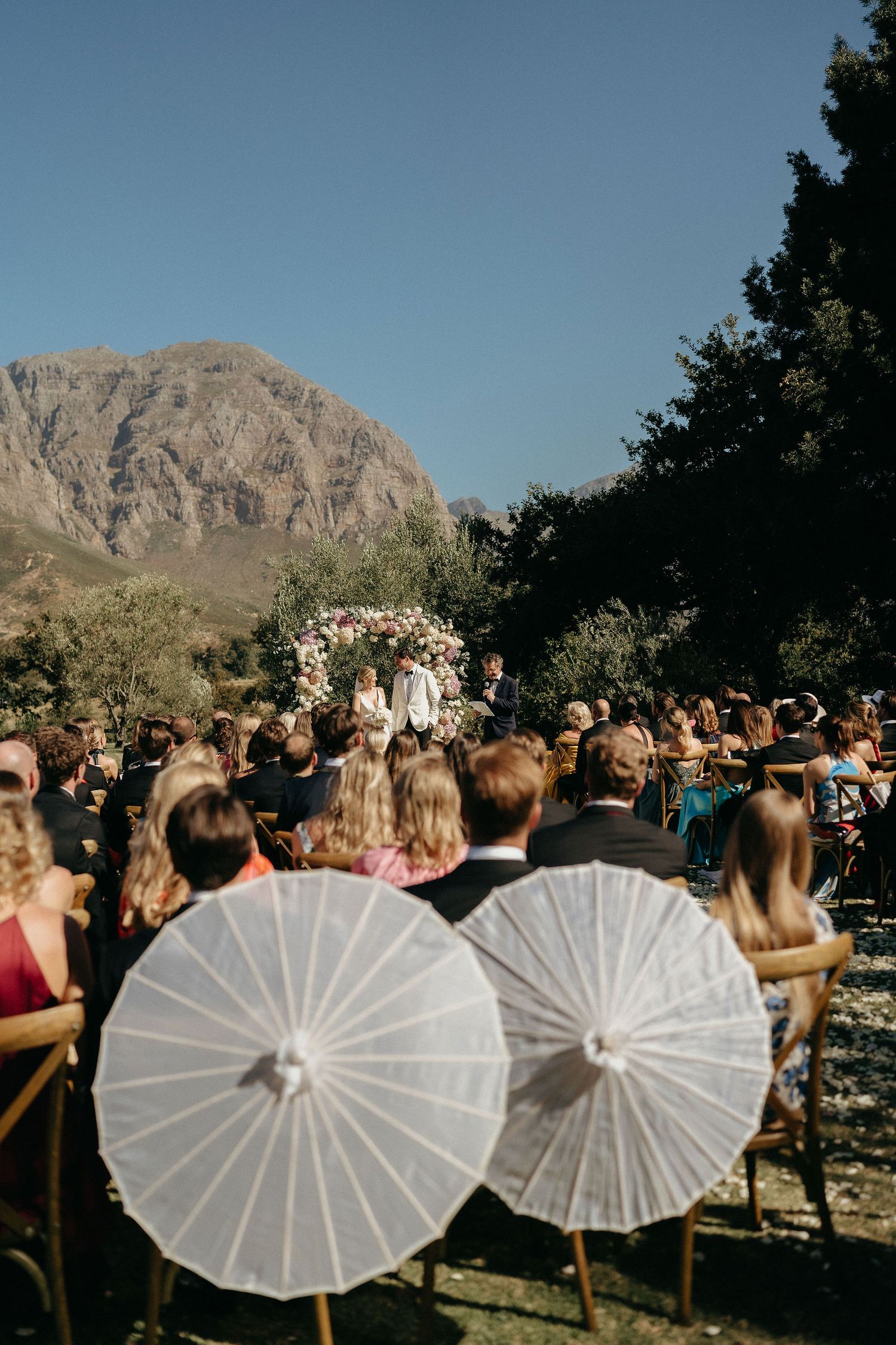 White parasols line up at an outdoor wedding ceremony with desert mountains and blue sky in the background.