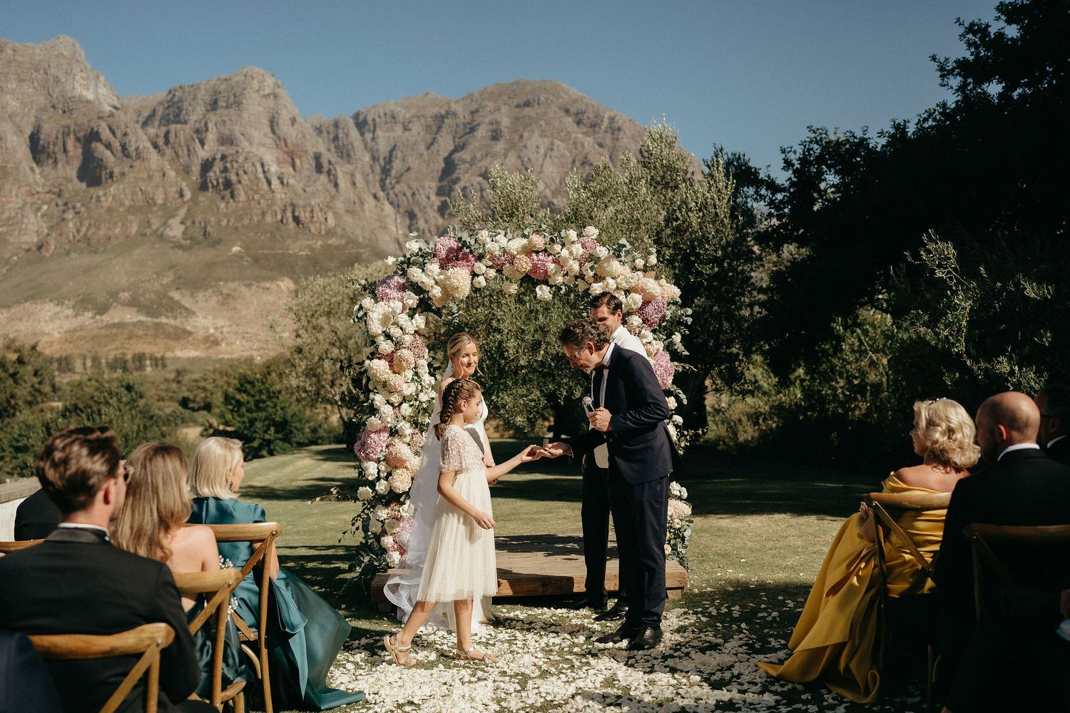 A panoramic wedding ceremony unfolds against a backdrop of majestic desert mountains and rugged cliffs.