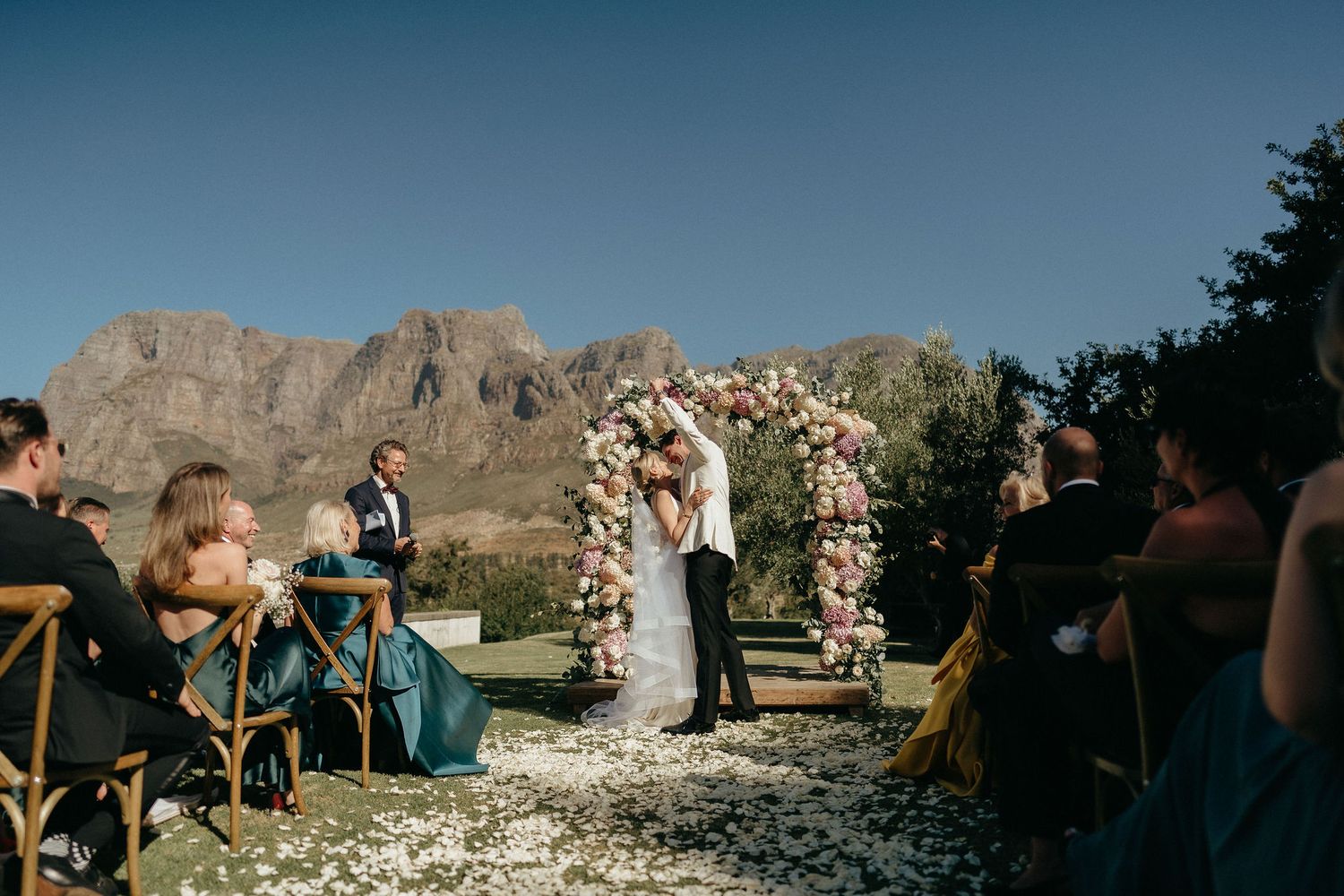 Panoramic view of a mountain wedding ceremony with guests seated in chairs against a dramatic desert landscape.