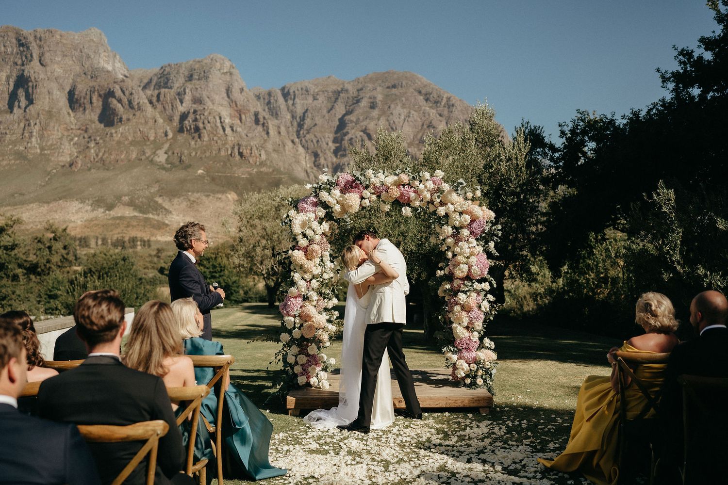 Wedding ceremony panorama with mountain backdrop and floral arch arrangements.
