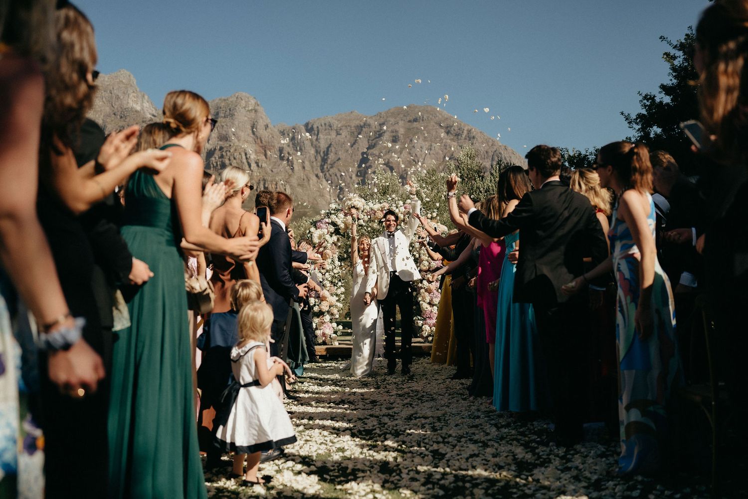 A wedding party in teal dresses stands on a rocky mountain overlook during an outdoor ceremony.