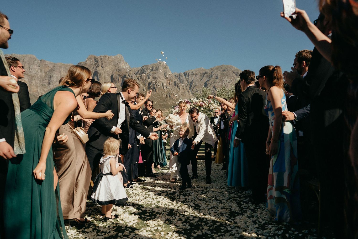 Wedding ceremony guests gather outdoors against a dramatic mountain backdrop in a scenic desert location.