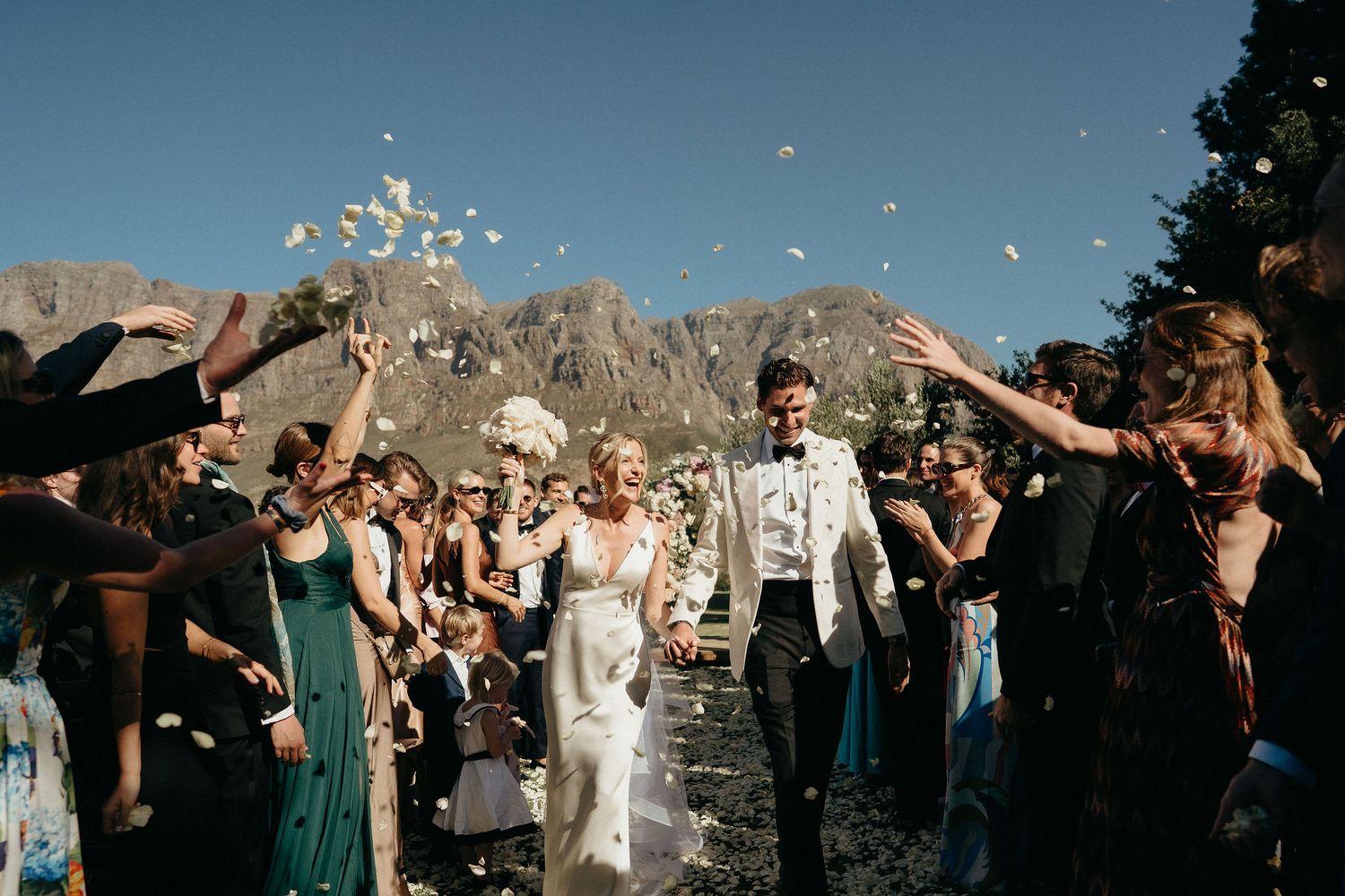 Wedding guests celebrate during an outdoor reception with sparklers at sunset against mountain backdrop.
