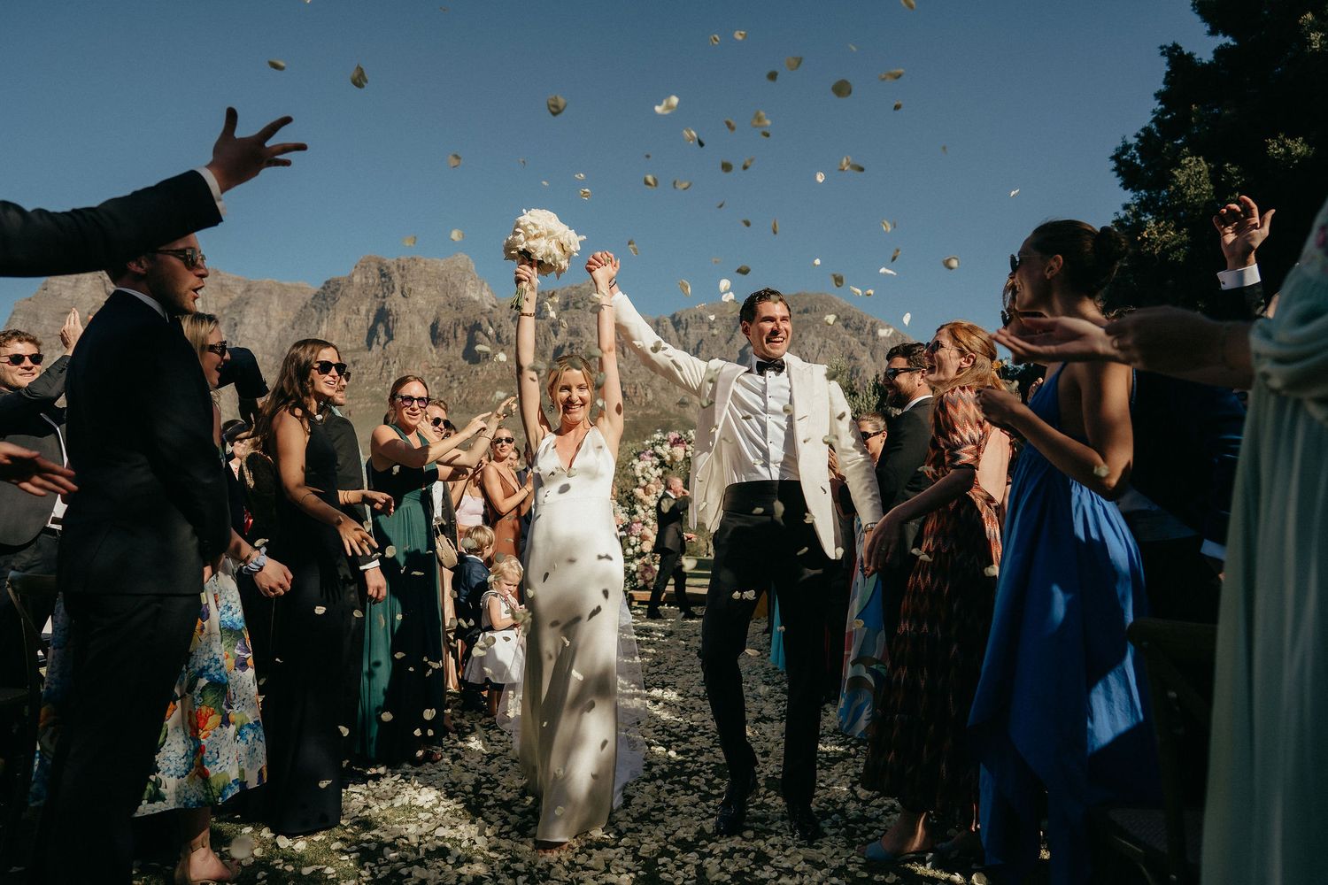 Wedding guests toss confetti in celebration against a backdrop of majestic mountain peaks.