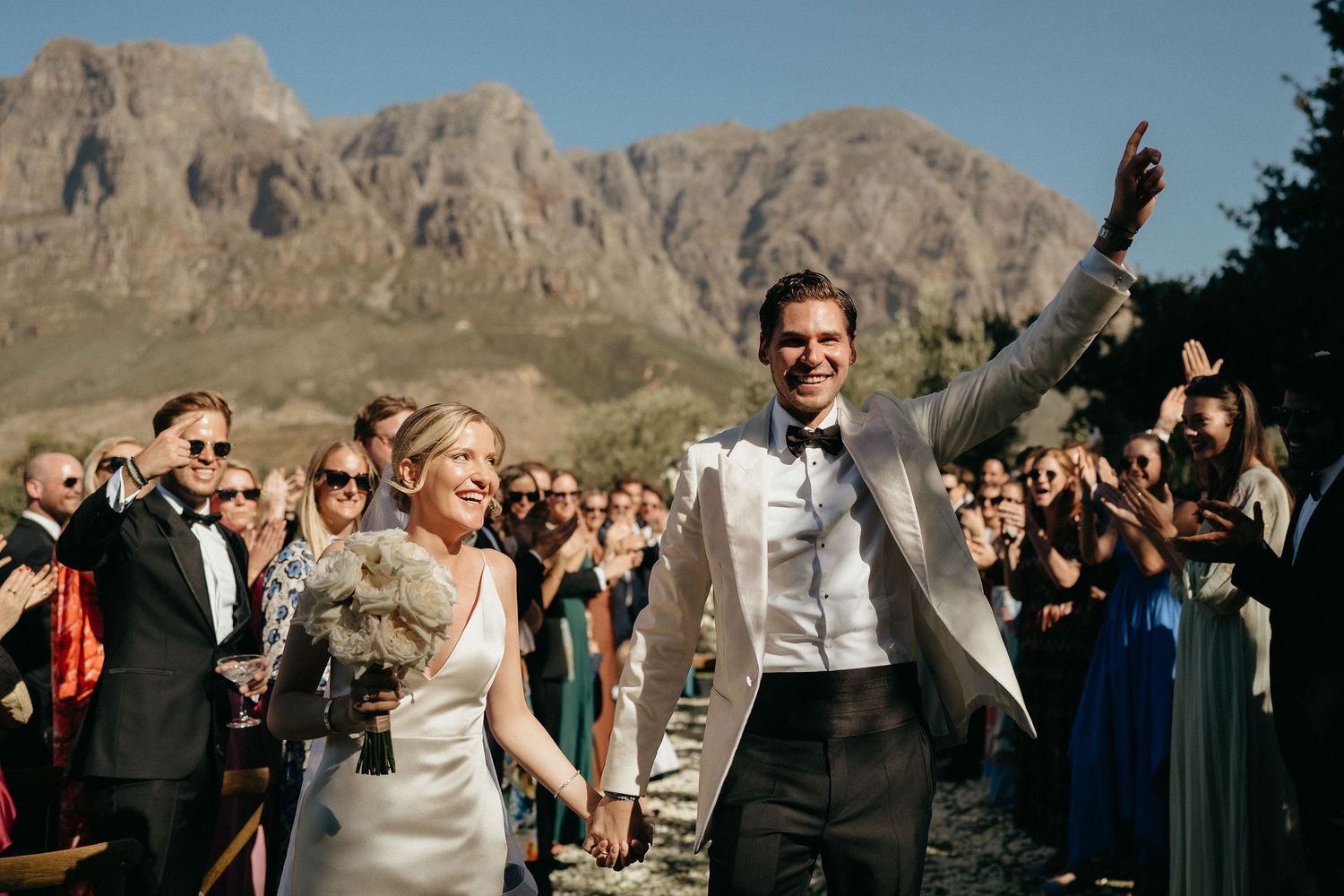 Outdoor wedding celebration with guests gathered beneath dramatic mountain scenery.