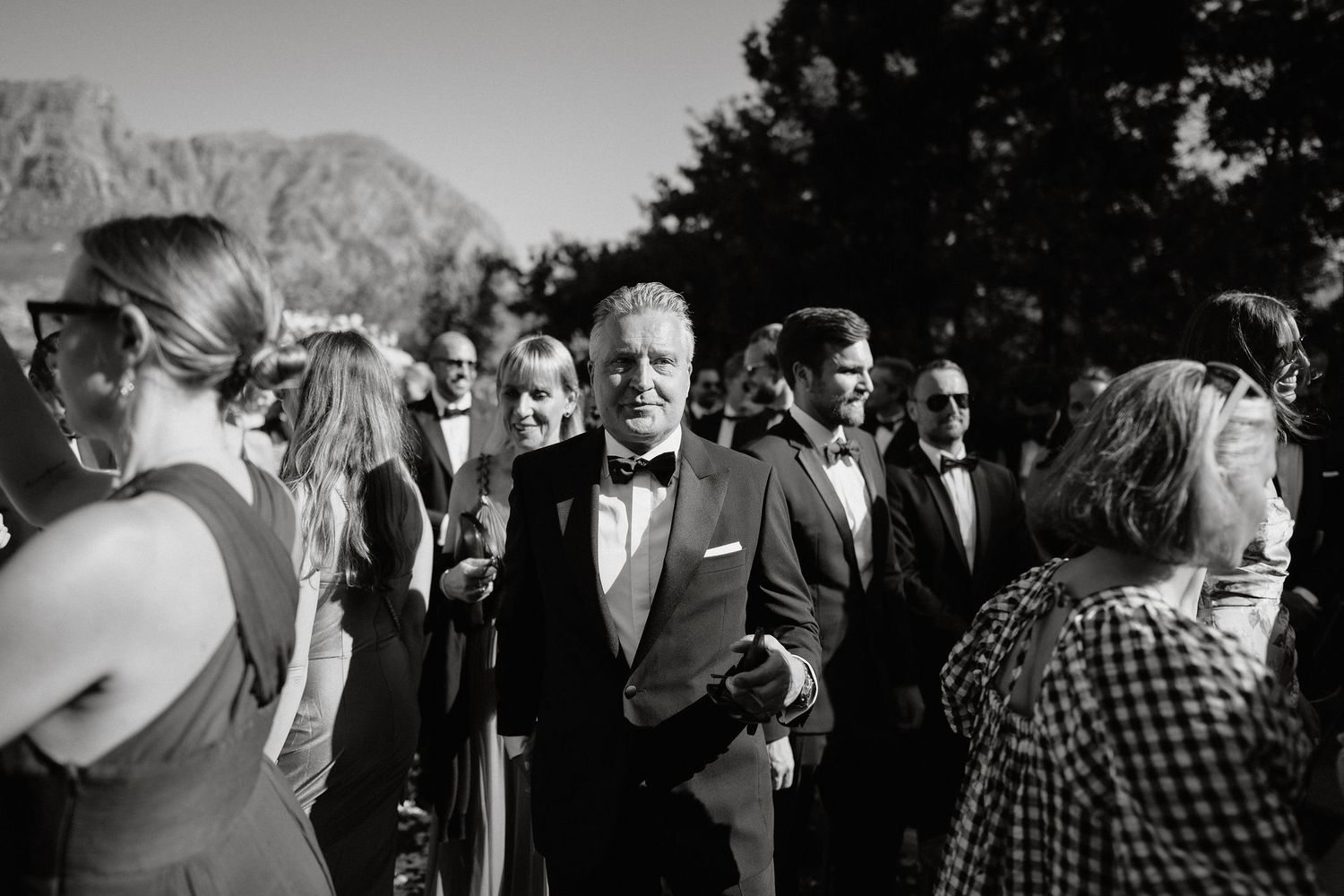 A collection of black and white candid wedding photos showing guests mingling and celebrating at an outdoor event.
