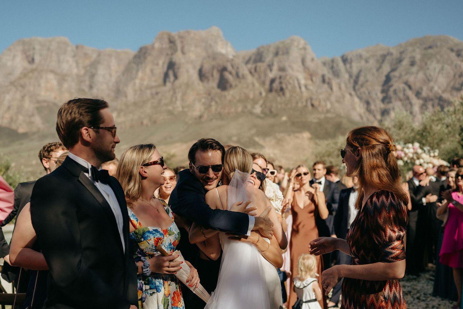 Wedding guests gather for an outdoor ceremony with scenic desert mountains and cliffs in the background.