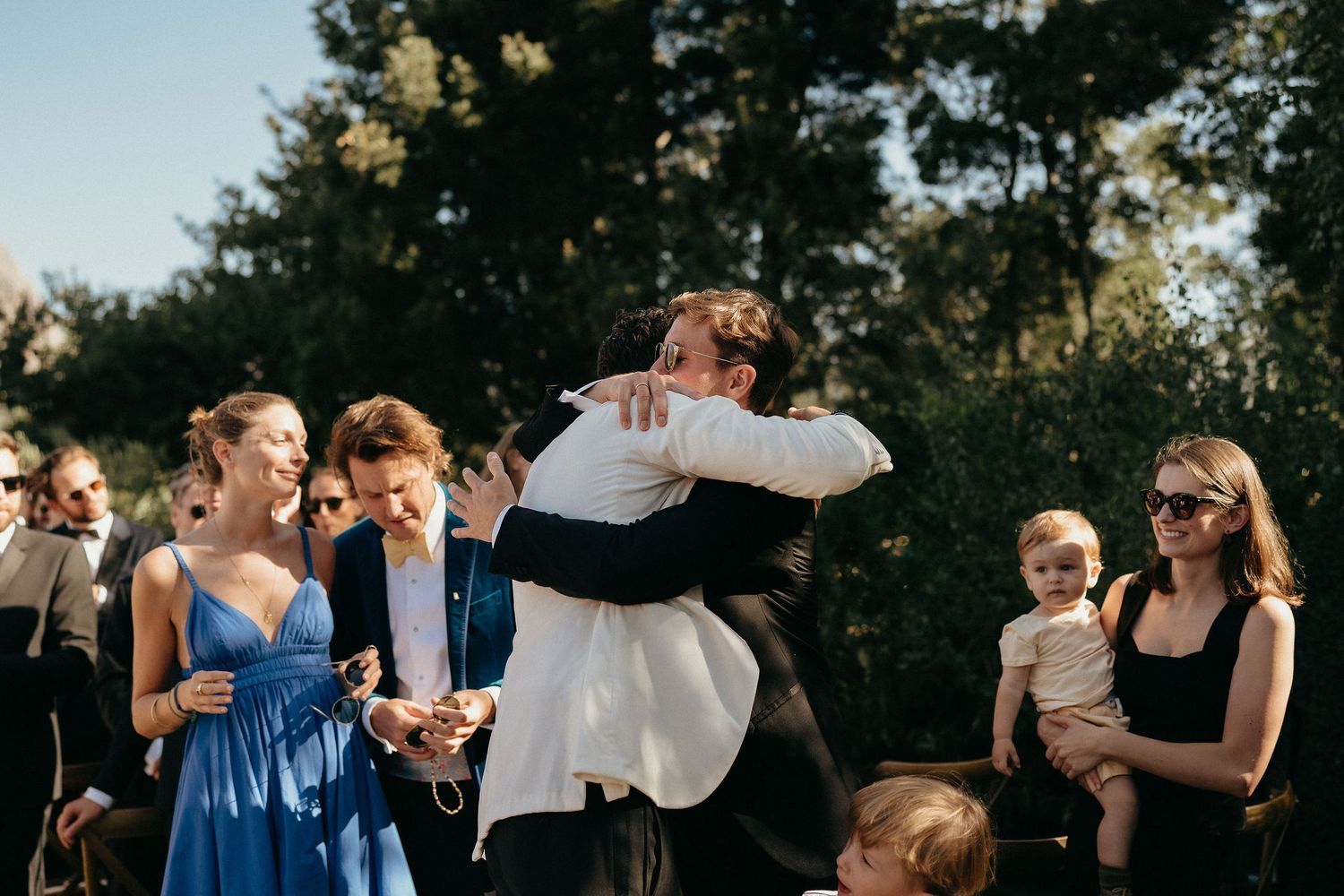 Wedding guests celebrate and dance together during an outdoor reception in a natural setting.