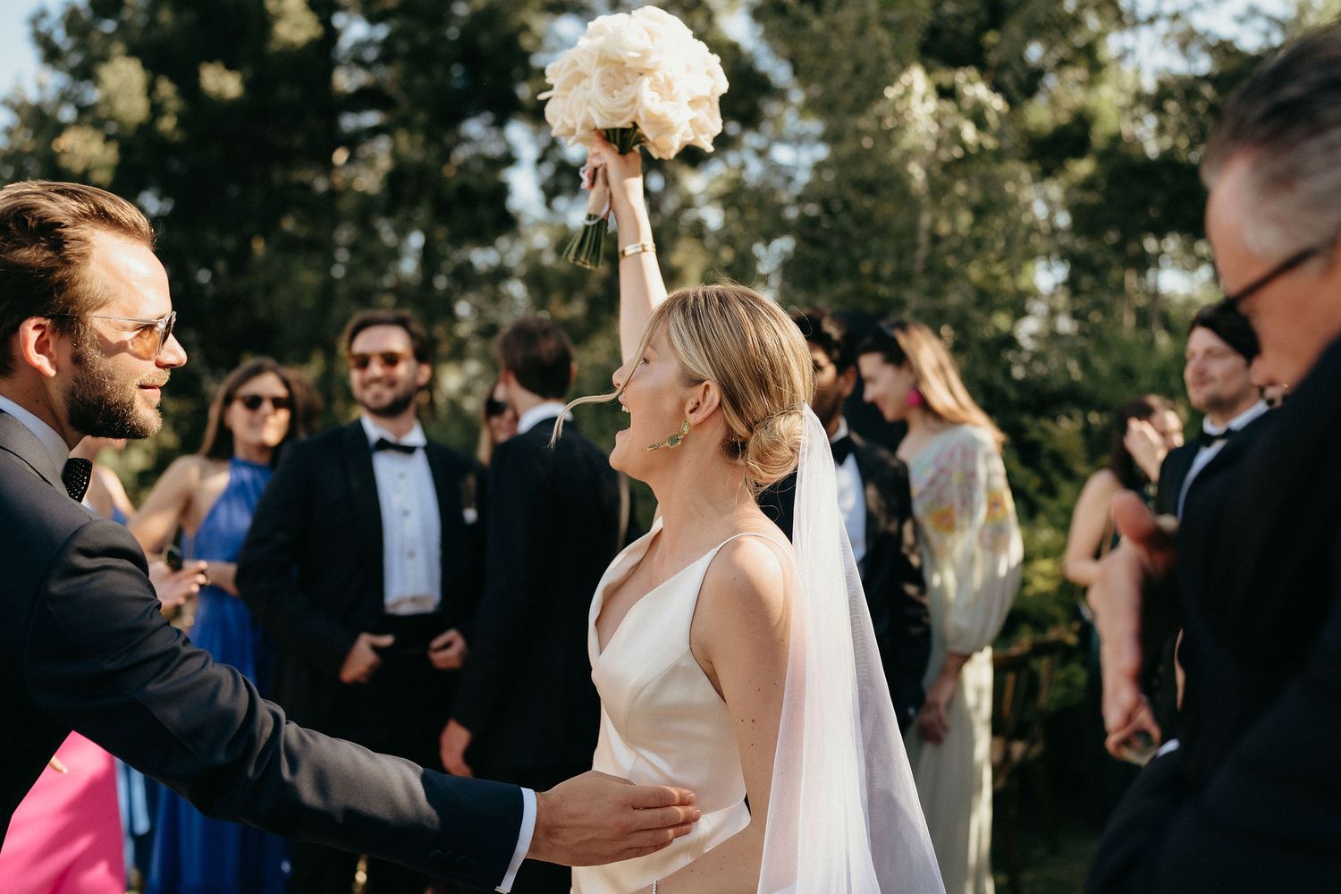A joyful outdoor wedding celebration with guests gathered around as newlyweds share a special moment in natural lighting.