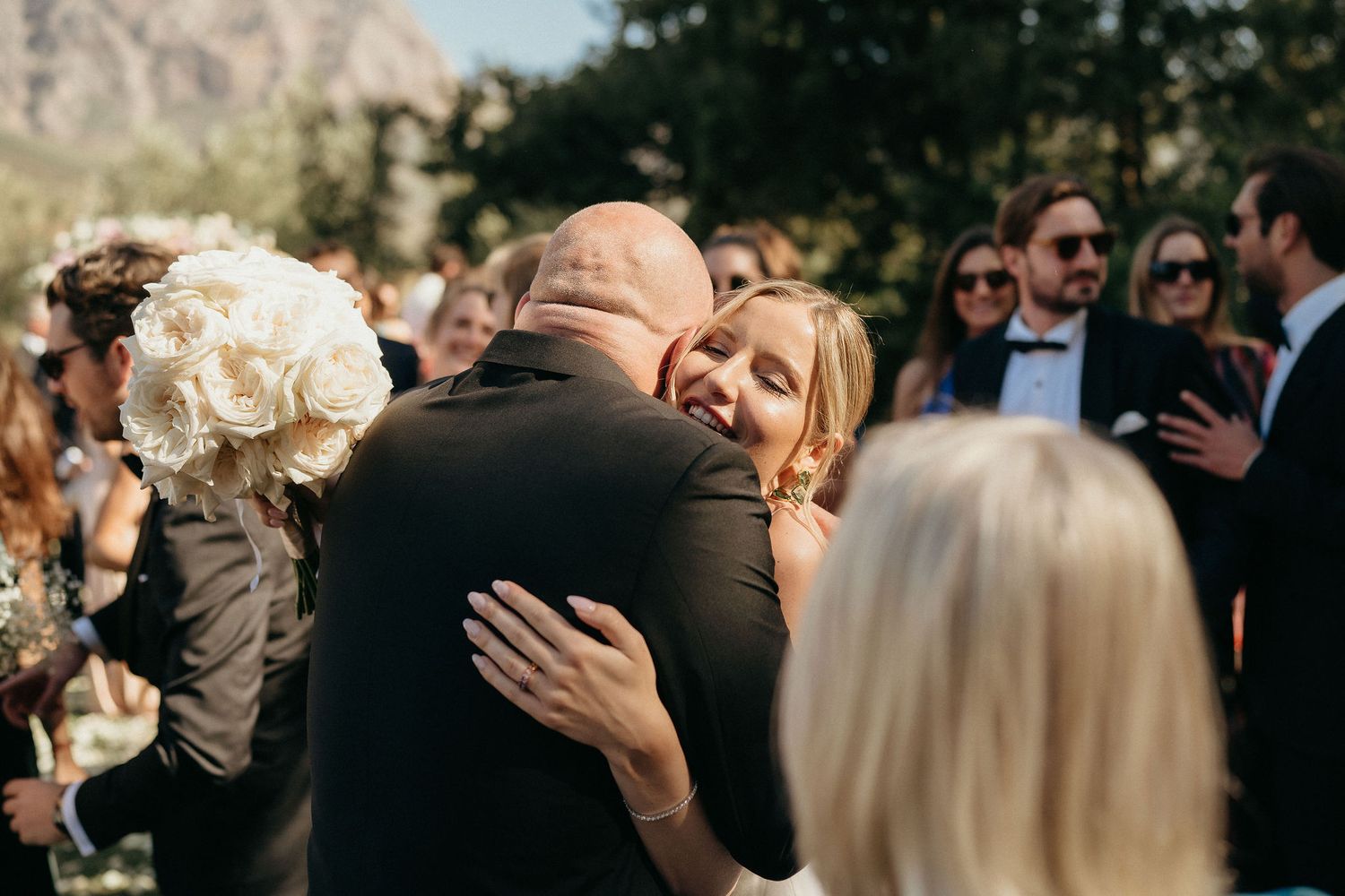 A series of candid moments from a wedding ceremony showing guests embracing and celebrating outdoors.