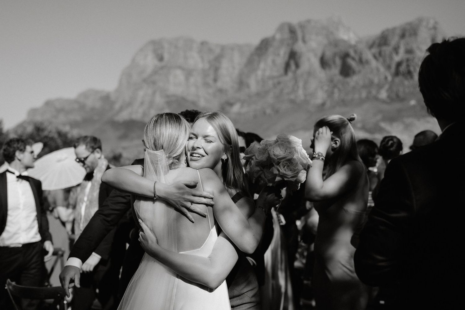 Black and white photo of a joyous outdoor wedding celebration with mountains in the background.