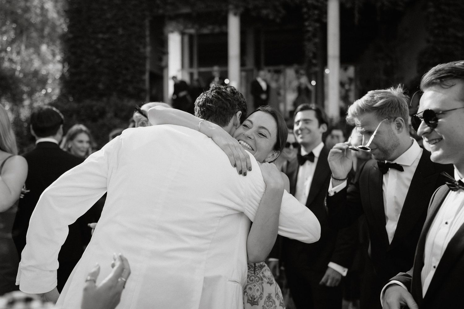 A black and white wedding photo showing guests dancing and celebrating at a reception party.