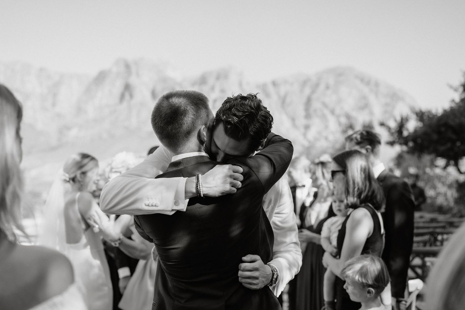 A tender embrace between two people at an outdoor wedding with mountains in the background.