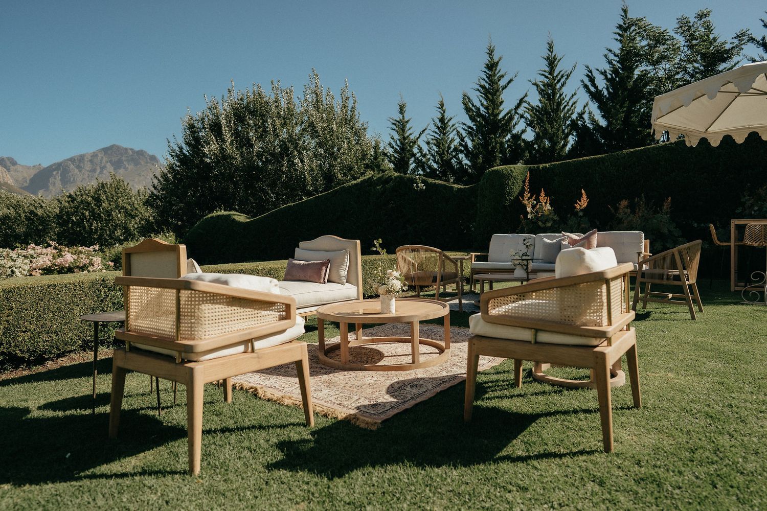 Wooden lounge chairs and benches arranged on a grassy lawn with mountains visible in the background.