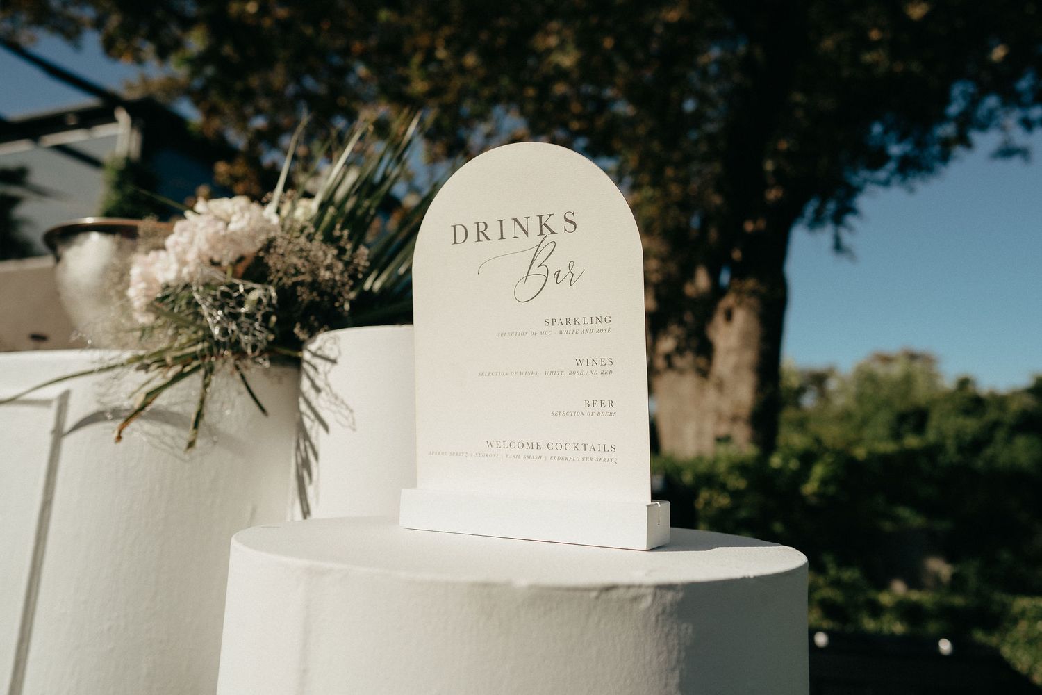 Elegant white wedding menu cards and floral arrangements displayed on a rustic wooden surface outdoors.