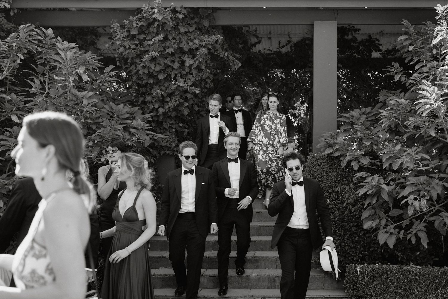 Wedding party standing in formal attire under trees during an outdoor ceremony.