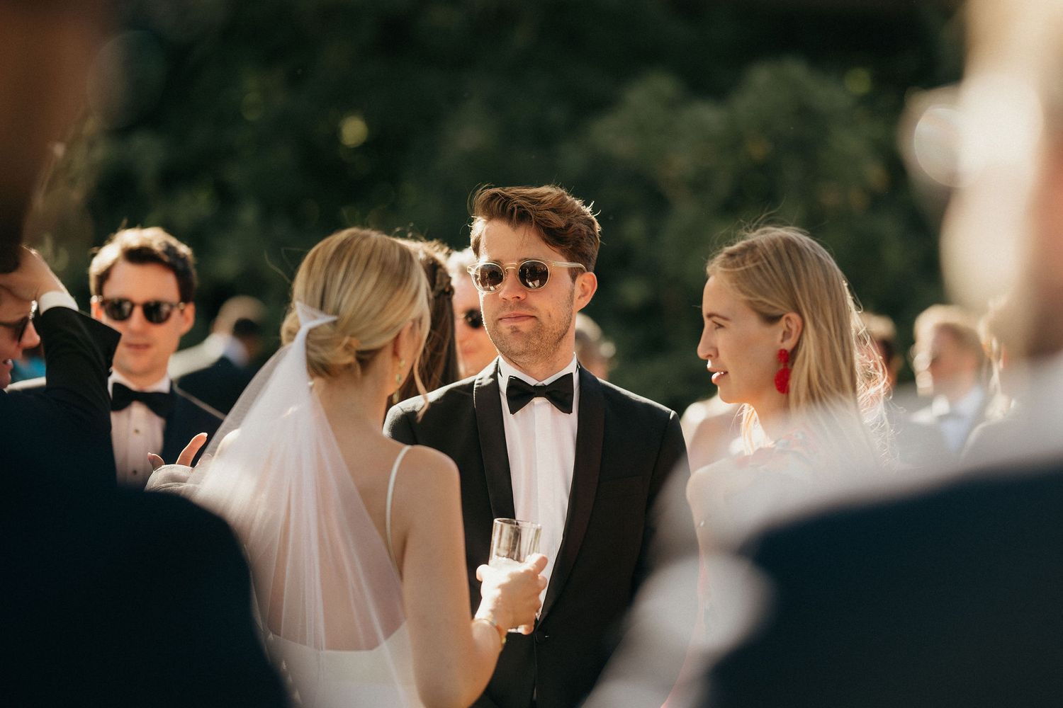 A romantic wedding reception outdoors with guests mingling and dancing at sunset.