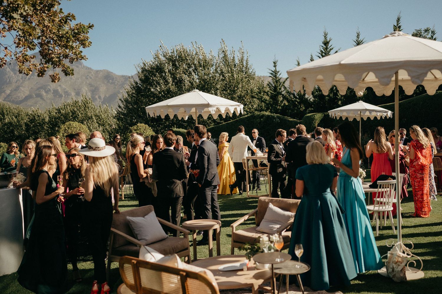 Outdoor wedding reception with guests mingling under white canopy tents at sunset with mountain views in background.