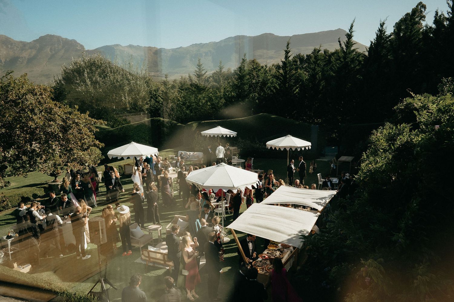 Panoramic view of an outdoor wedding venue with white tents and mountains in the background during sunset.