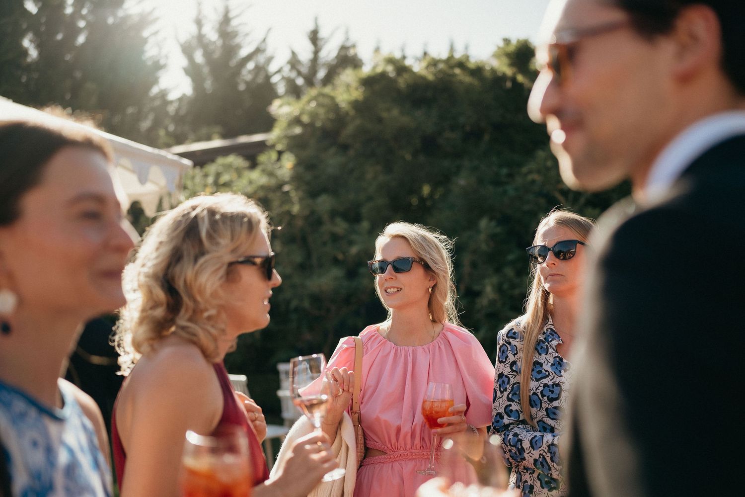 Wedding guests in colorful summer attire gather outdoors during a celebration on a sunny afternoon.