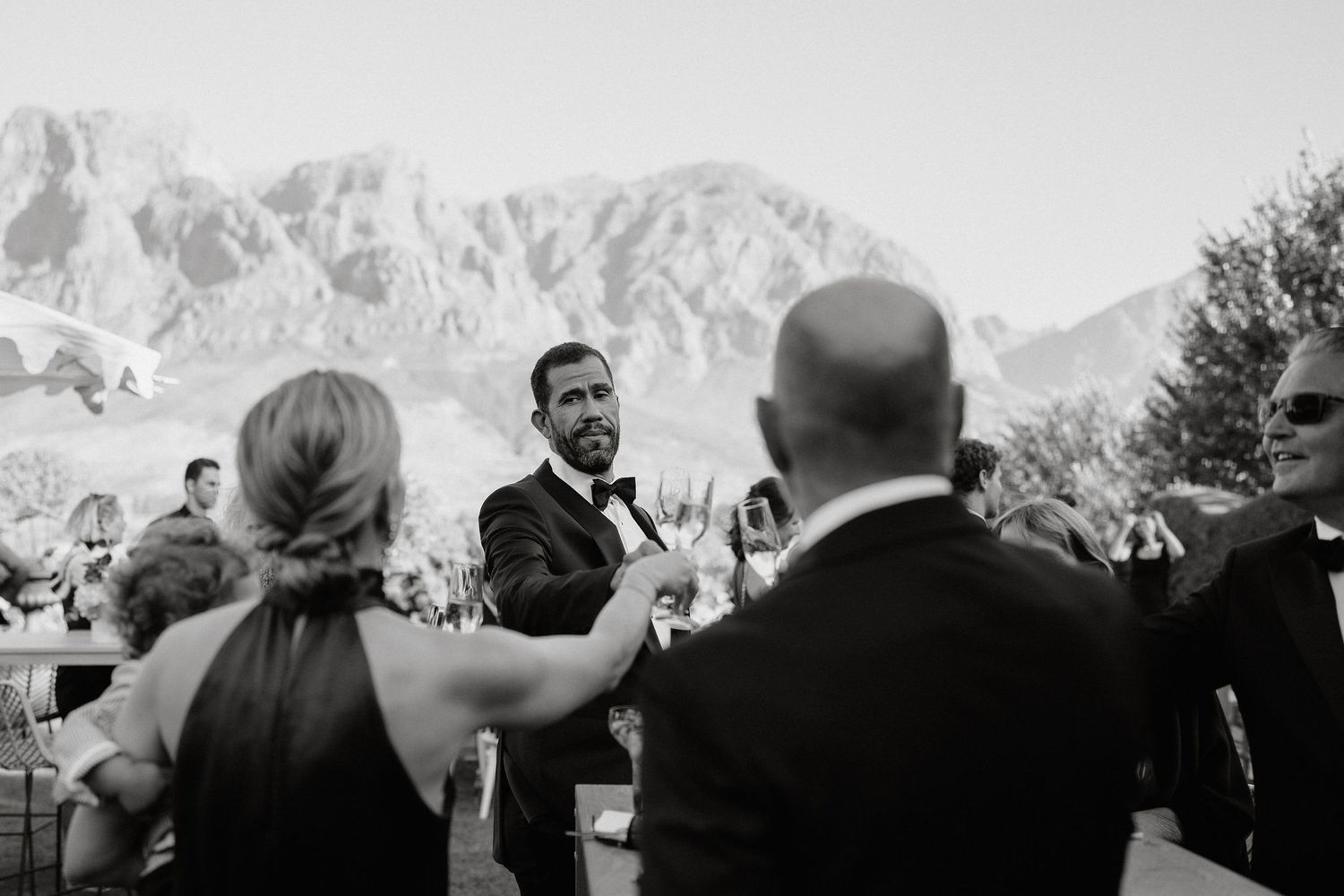 A sequence of black and white wedding photos showing guests and celebrations against a mountain backdrop.