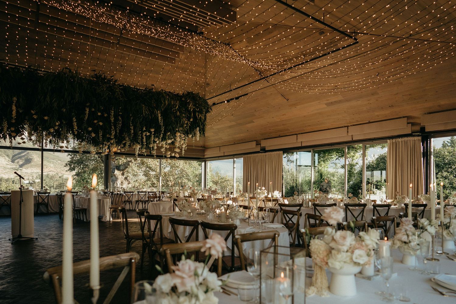 Elegant wedding reception venue with hanging floral arrangements and white table settings in a rustic indoor space.