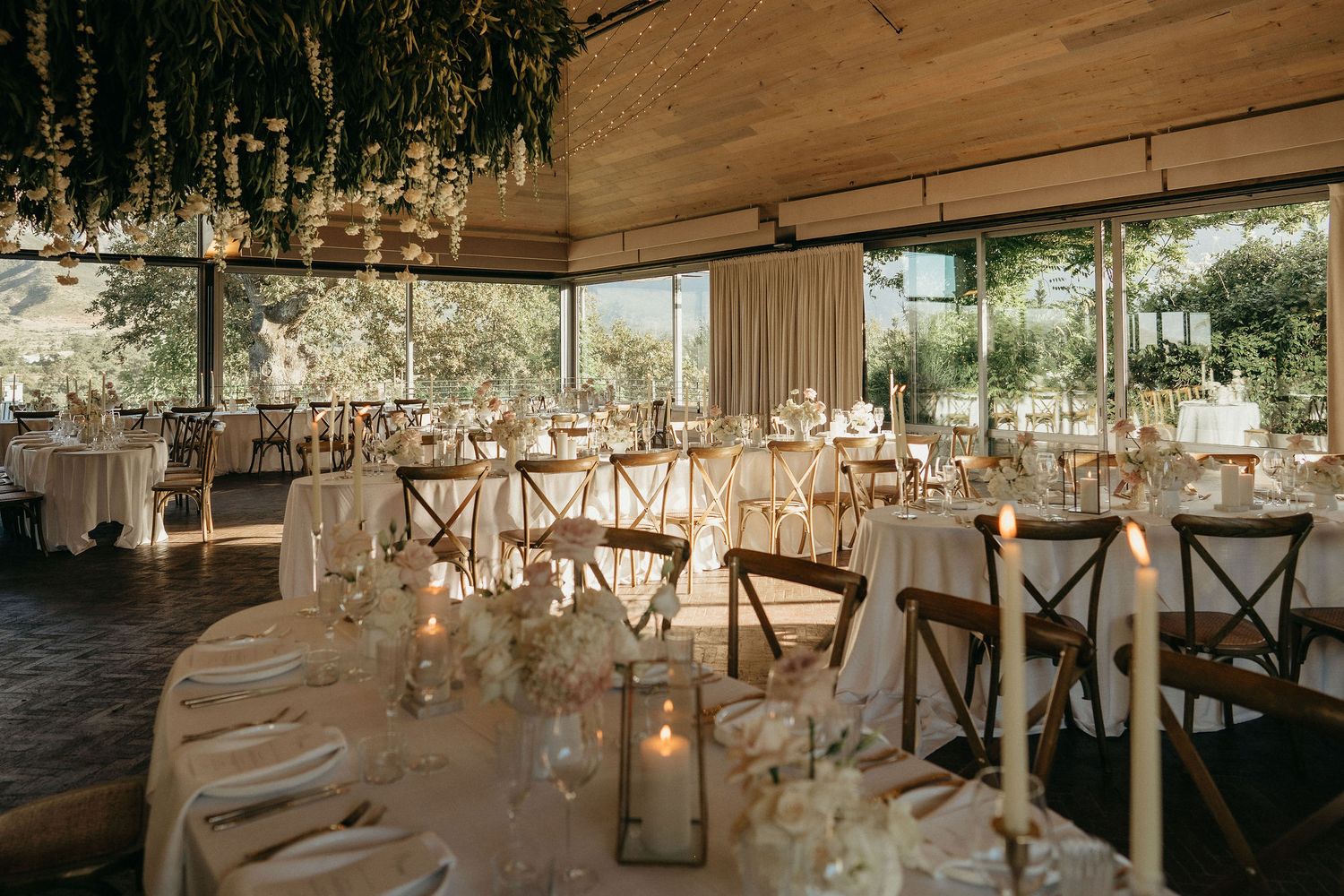 Elegant wedding reception venue with rustic wooden tables and hanging floral arrangements under a covered outdoor space.