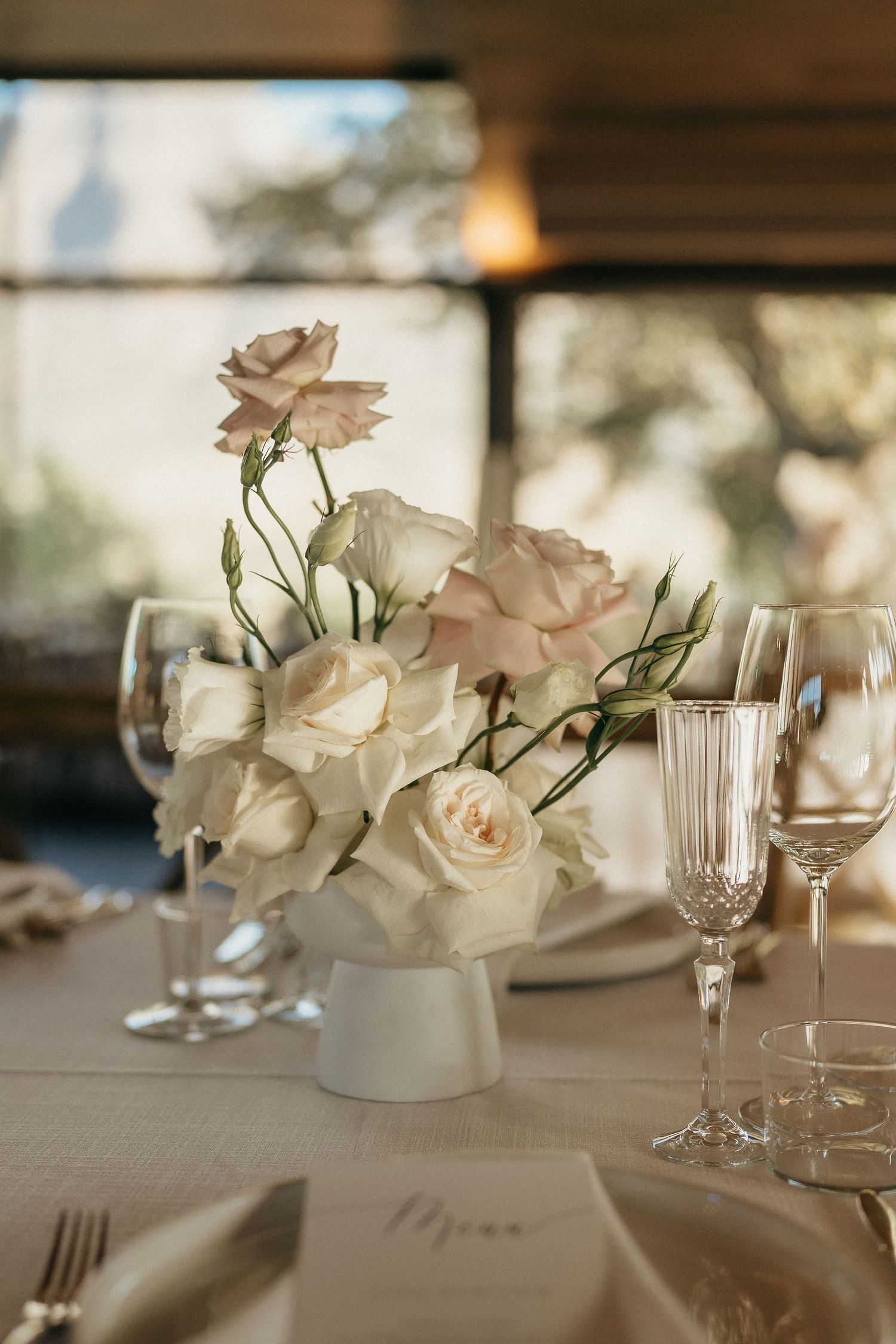 Elegant white roses in small vases decorate a formal dining table with wine glasses and place settings.