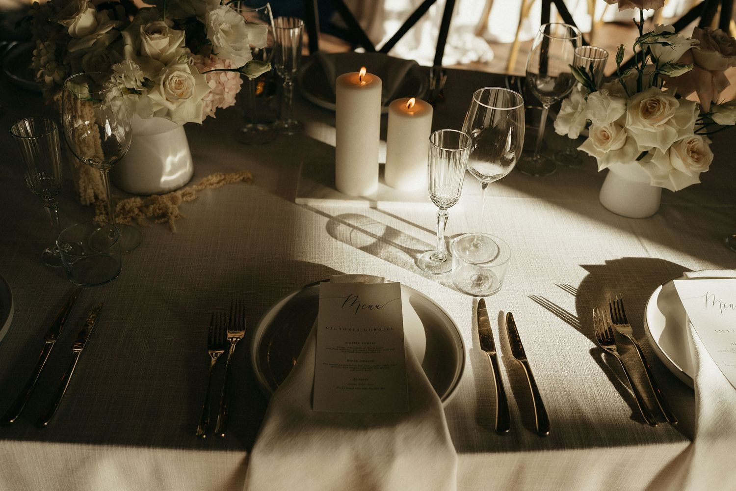 White floral arrangements and candles decorate elegant wedding reception tables with soft lighting and romantic ambiance.