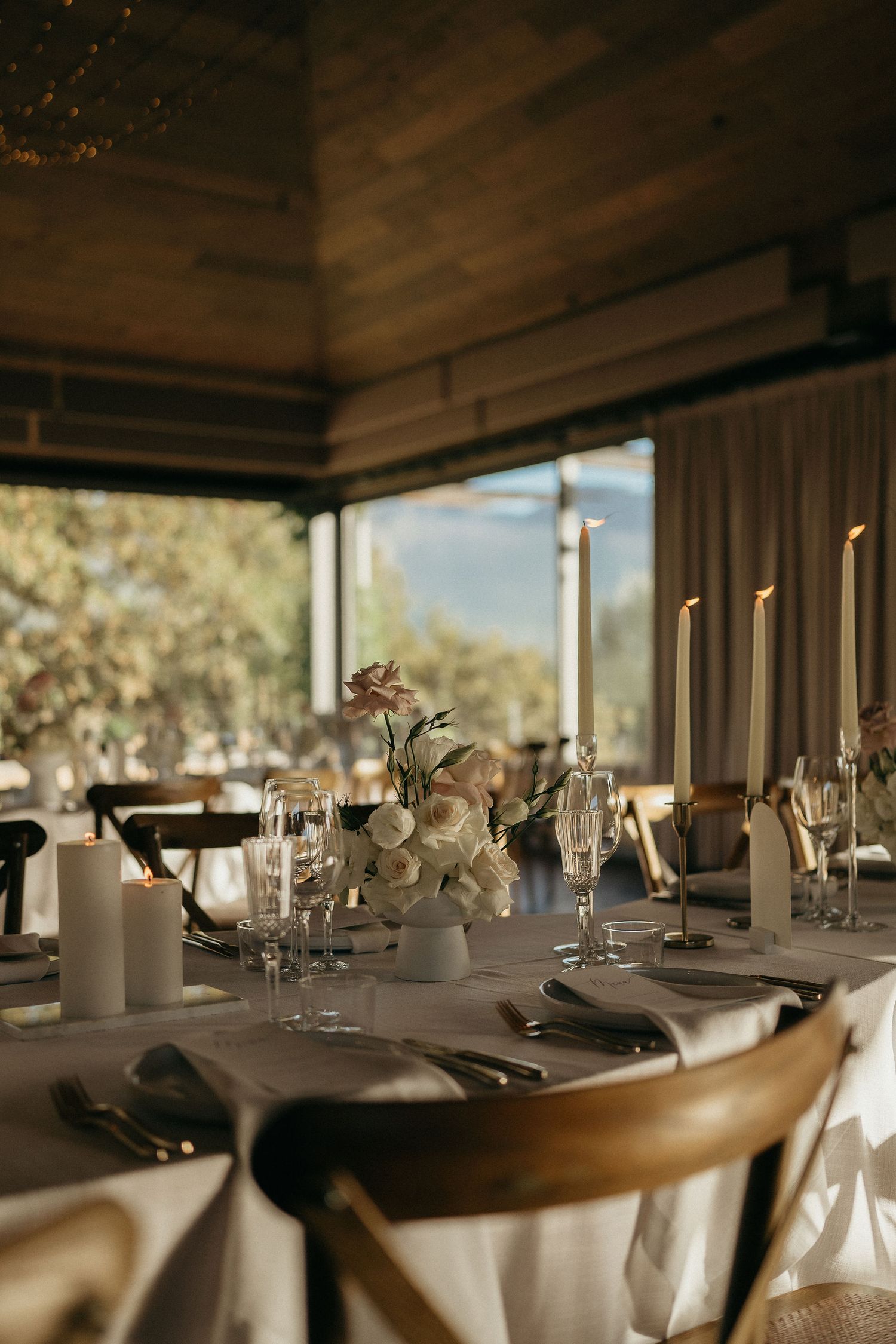 Elegant table settings with white candles and floral centerpieces in a modern dining room with natural lighting.