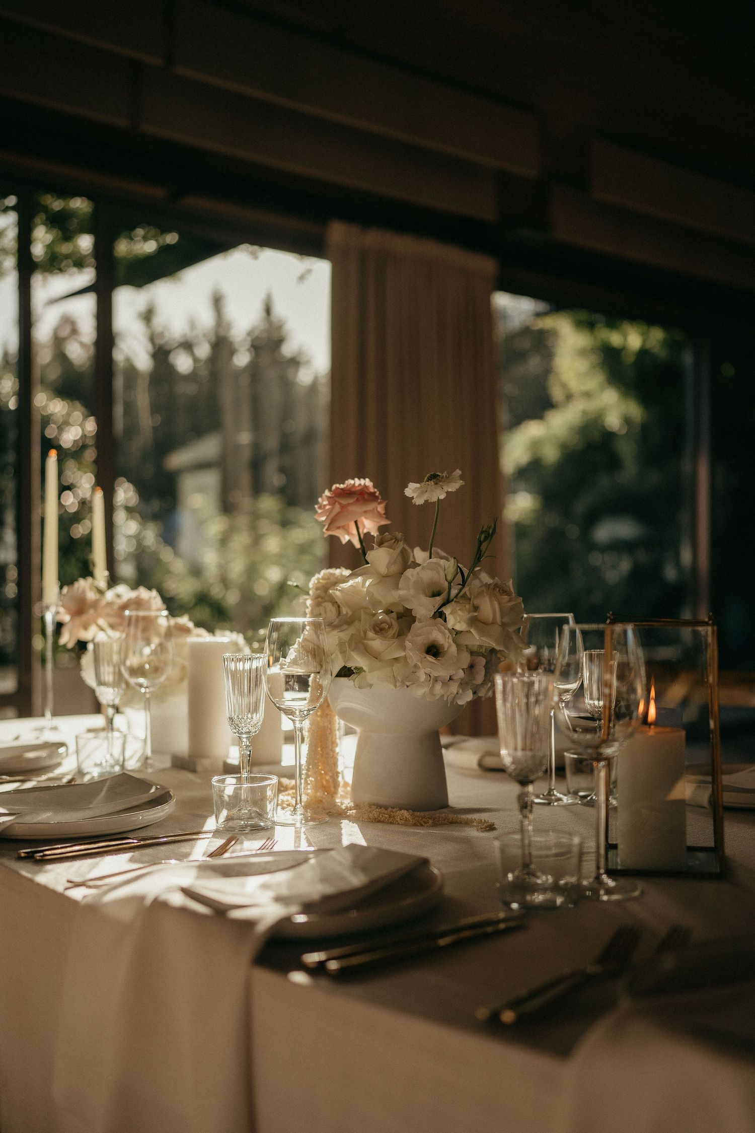 Elegant wedding reception tables set with white floral centerpieces and glassware in warm natural lighting.