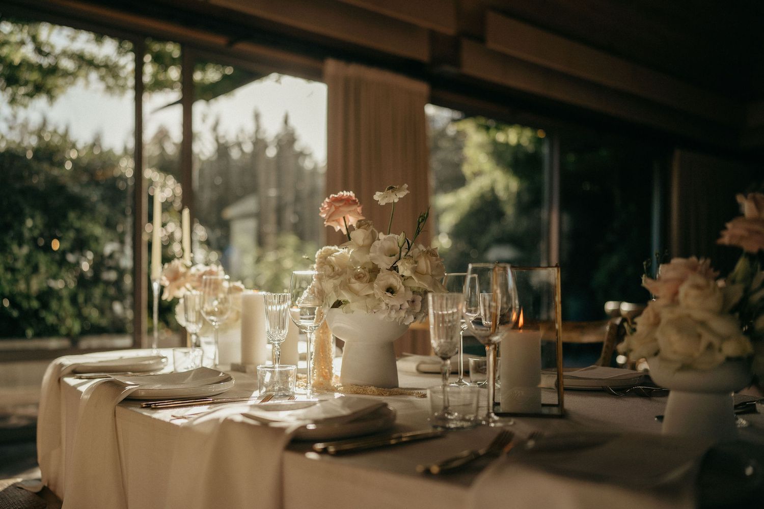 Elegant wedding reception table settings with glowing candles and glassware in warm evening light.