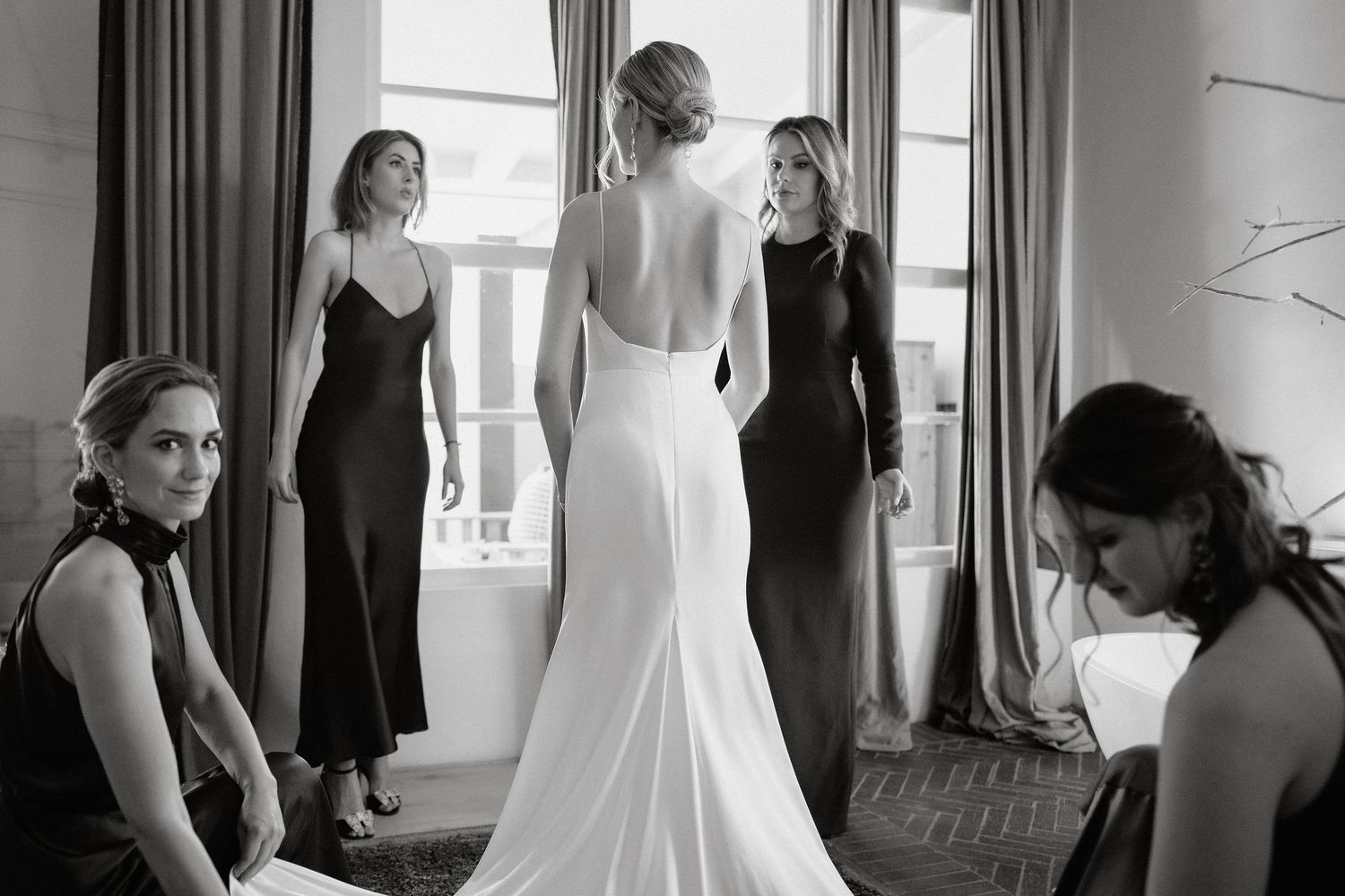 A series of black and white wedding preparation photos showing dress adjustments and candid moments.