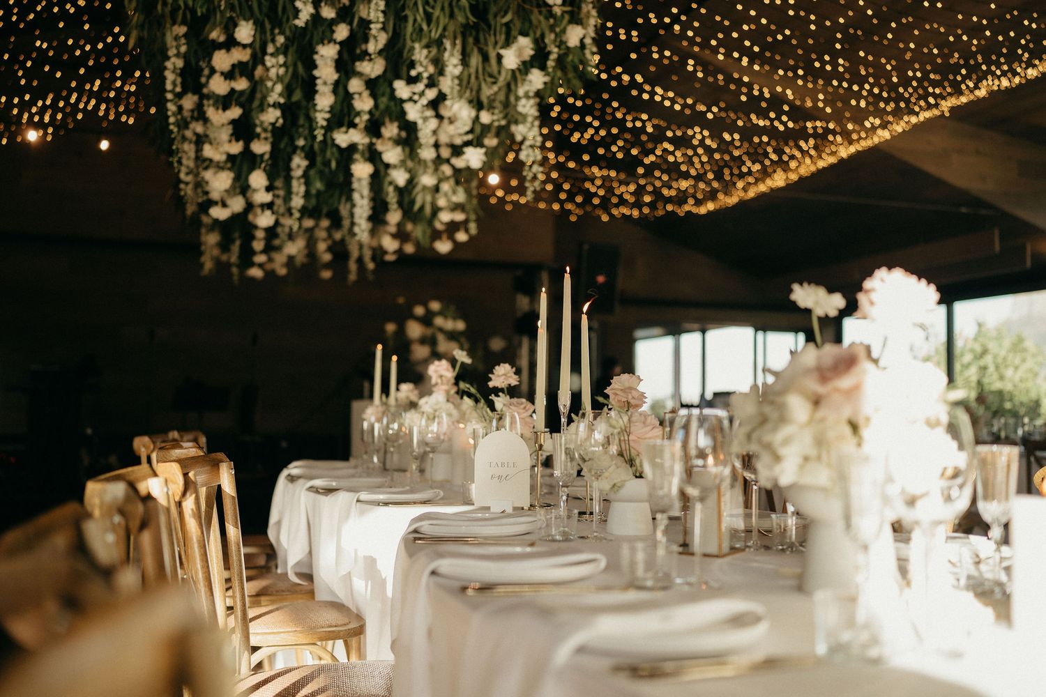 A romantic wedding reception venue decorated with twinkling string lights and white floral centerpieces on elegant tables.