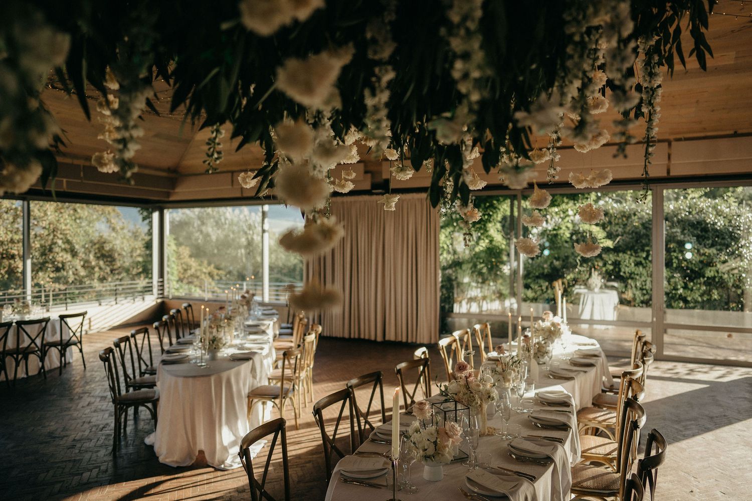 Elegant wedding reception venue with rustic chairs and hanging greenery in a sunlit covered outdoor space.
