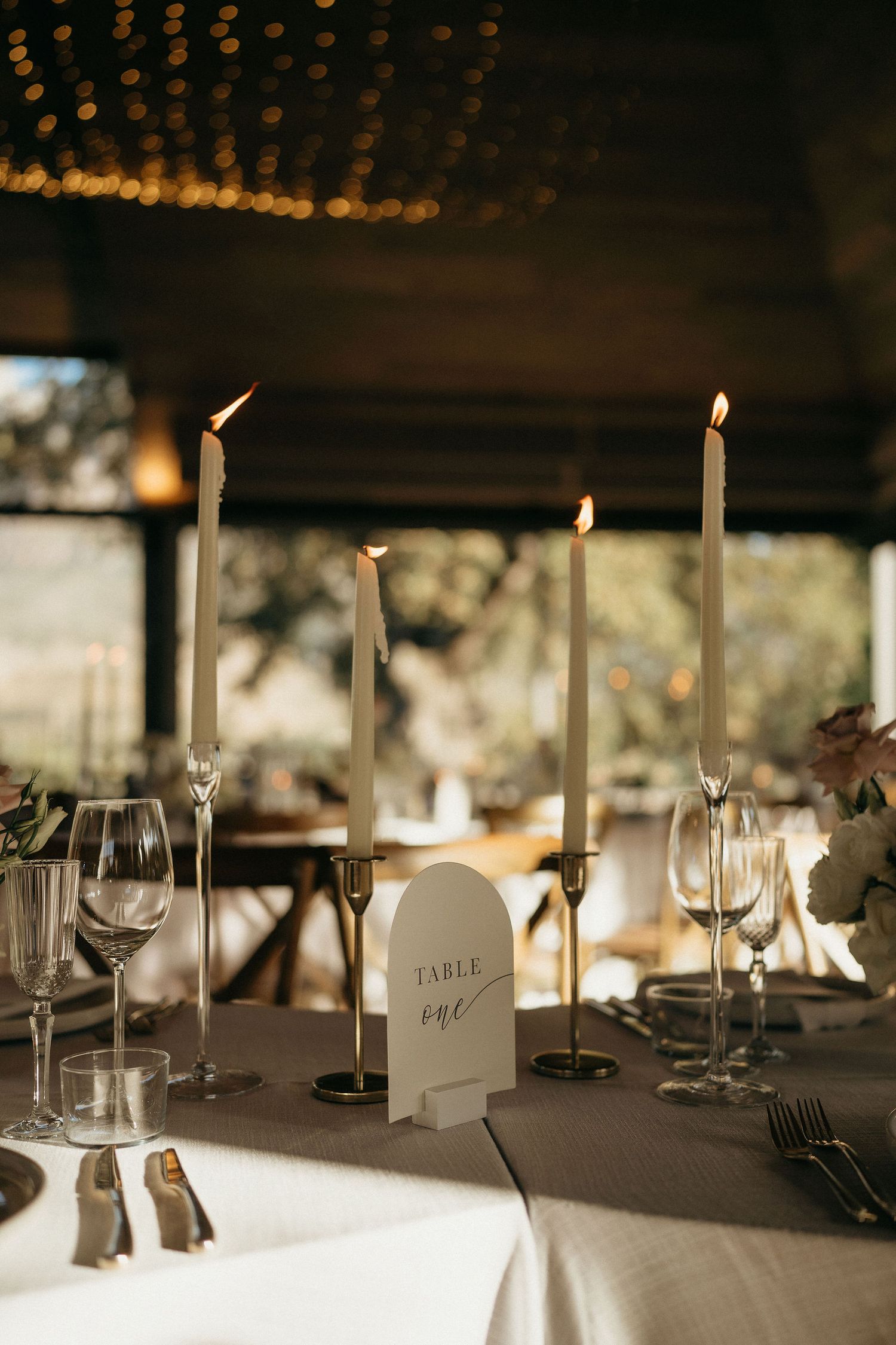 Elegant wedding reception table settings with white taper candles and soft lighting creating a romantic ambiance.