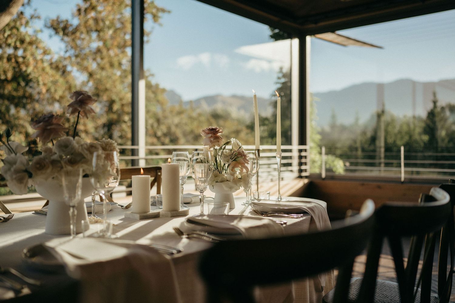 Elegant table settings and wine glasses arranged on a covered outdoor patio with mountain views in the background.