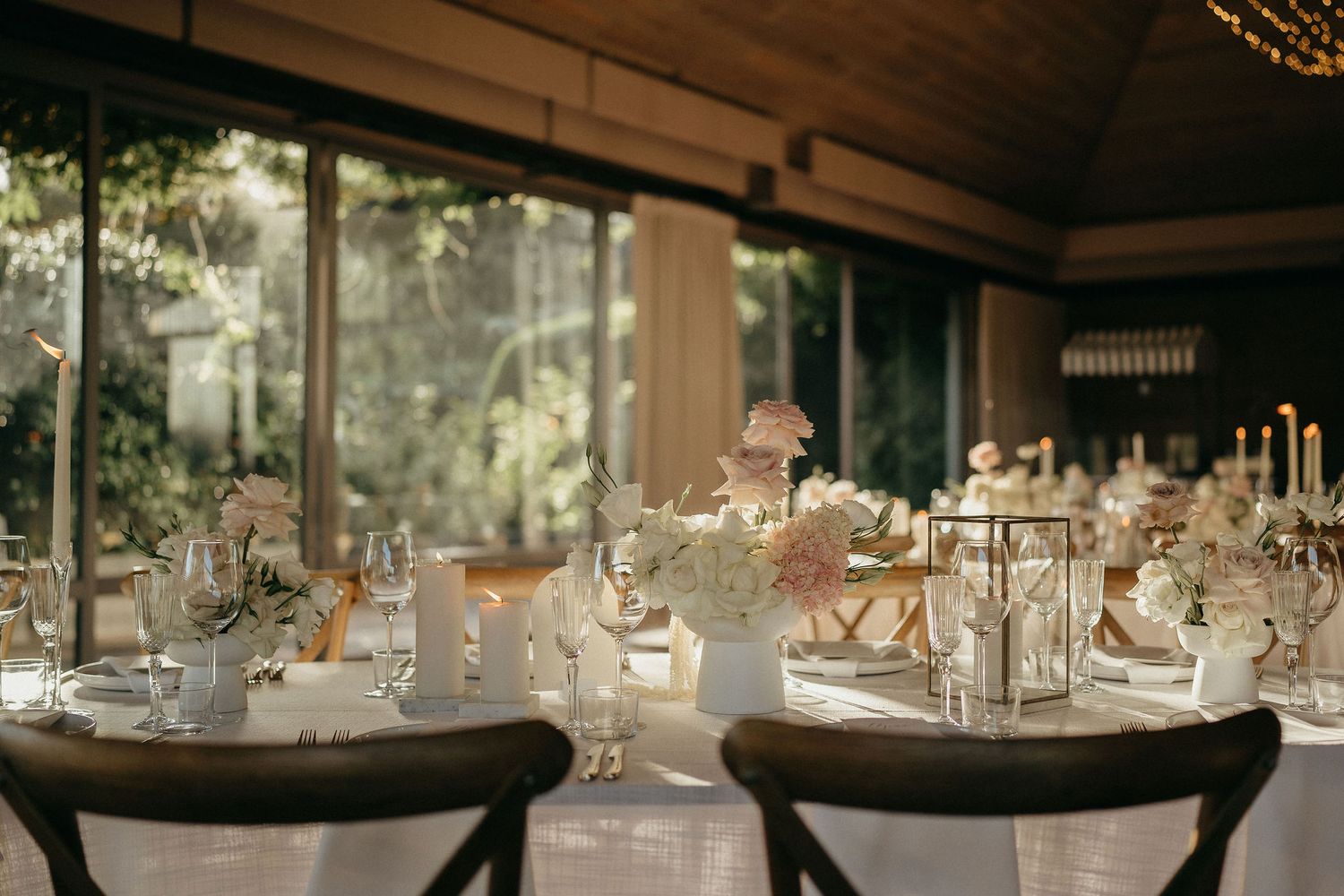 Elegant wedding reception tables set with candles and floral centerpieces in a rustic indoor venue with natural lighting.